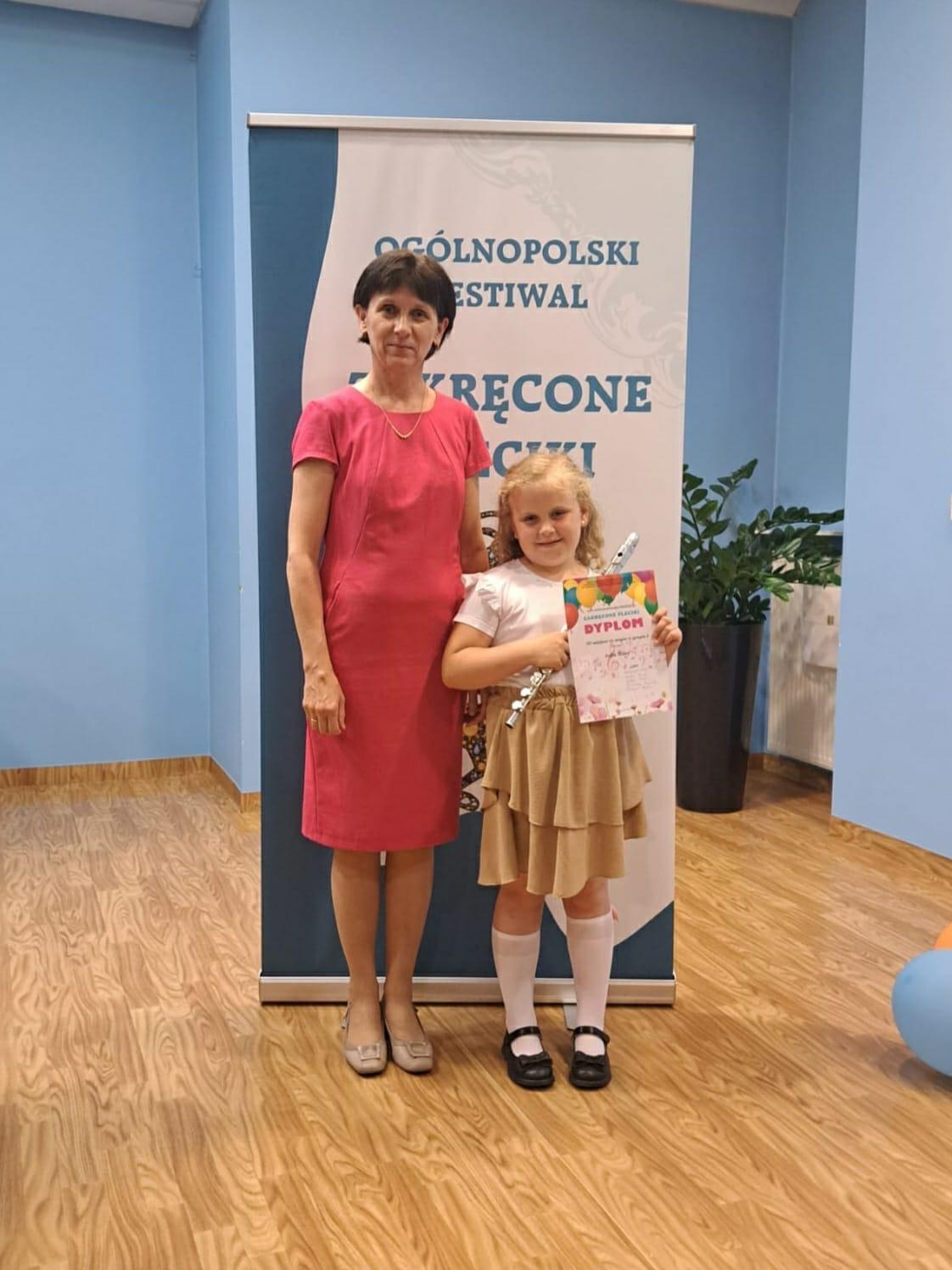 Zdjęcie przedstawia panią nauczycielkę ora uczennicę z instrumentem i dyplomem w rękach. 