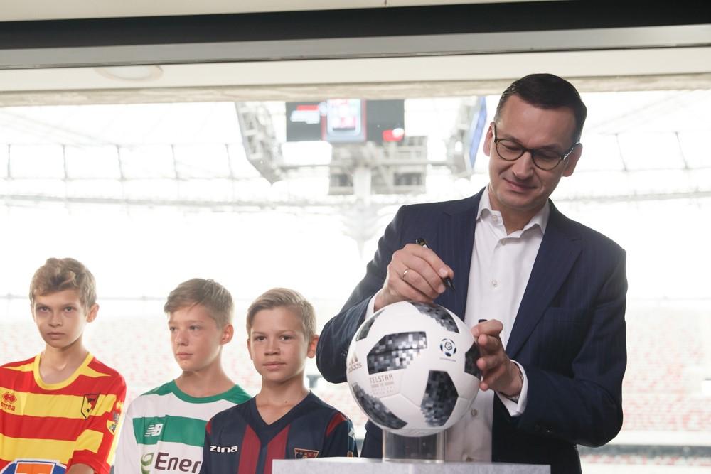 Premier Mateusz Morawiecki i stoi na zdjęciu grupowym z młodymi piłkarzami.