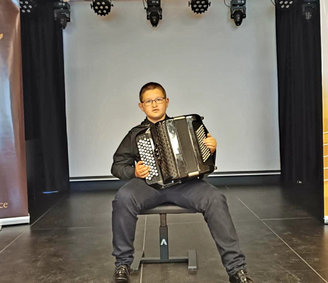 Zdjęcie - Krystian Śmiertka. Uczeń siedzi na krześle, trzyma guzikowy akordeon