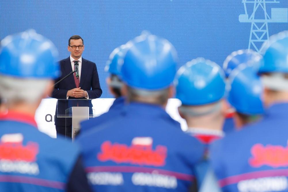 Premier Mateusz Morawiecki przemawia przed robotnikami w kaskach.