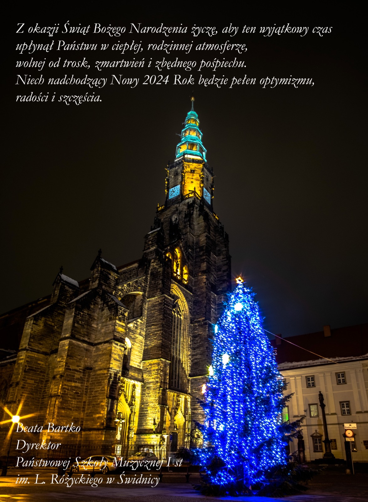 Zdjęcie nocne katedry świdnickiej po prawej niebieska choinka . Na tym tle białe napisy z życzeniami - czcionka ozdobna