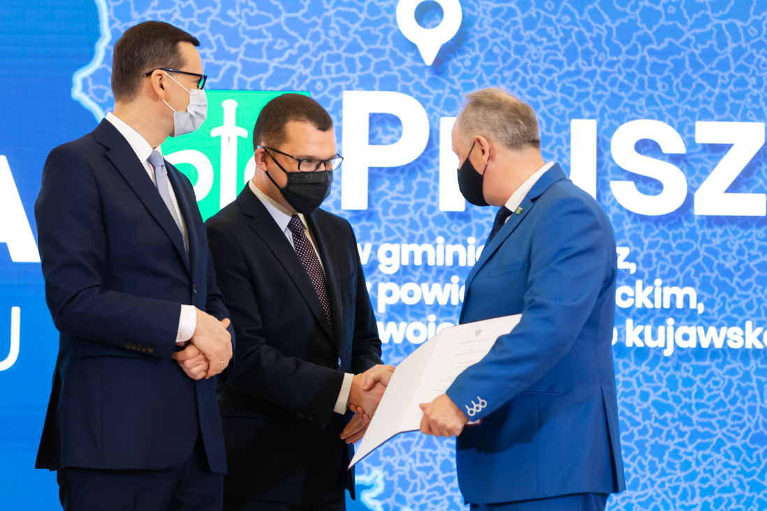 Na zdjęciu widać premiera Mateusza Morawieckiego i wiceministra Pawła Szefernakera składającego gratulacje jednemu z przedstawicieli gmin która otrzymała akt nadania statusu miasta.