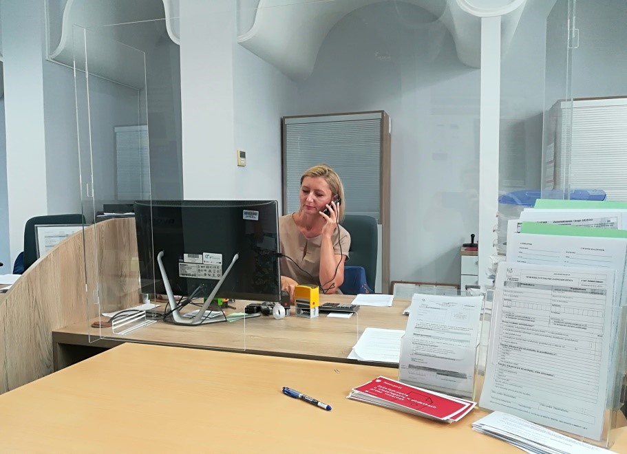 ​Wnętrze Urzędu Skarbowego w Międzyrzeczu, przy stanowisku dla obsługi klienta siedzi kobieta i rozmawia przez telefon