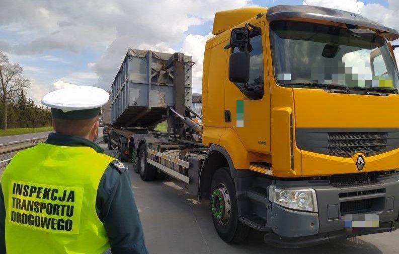 Inspektor stoi koło przeładowywanej ciężarówki z kontenerami.