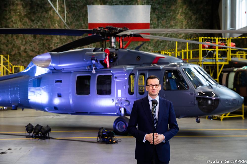 Premier Mateusz Morawiecki przemawia, a w tle stoi śmigłowiec.