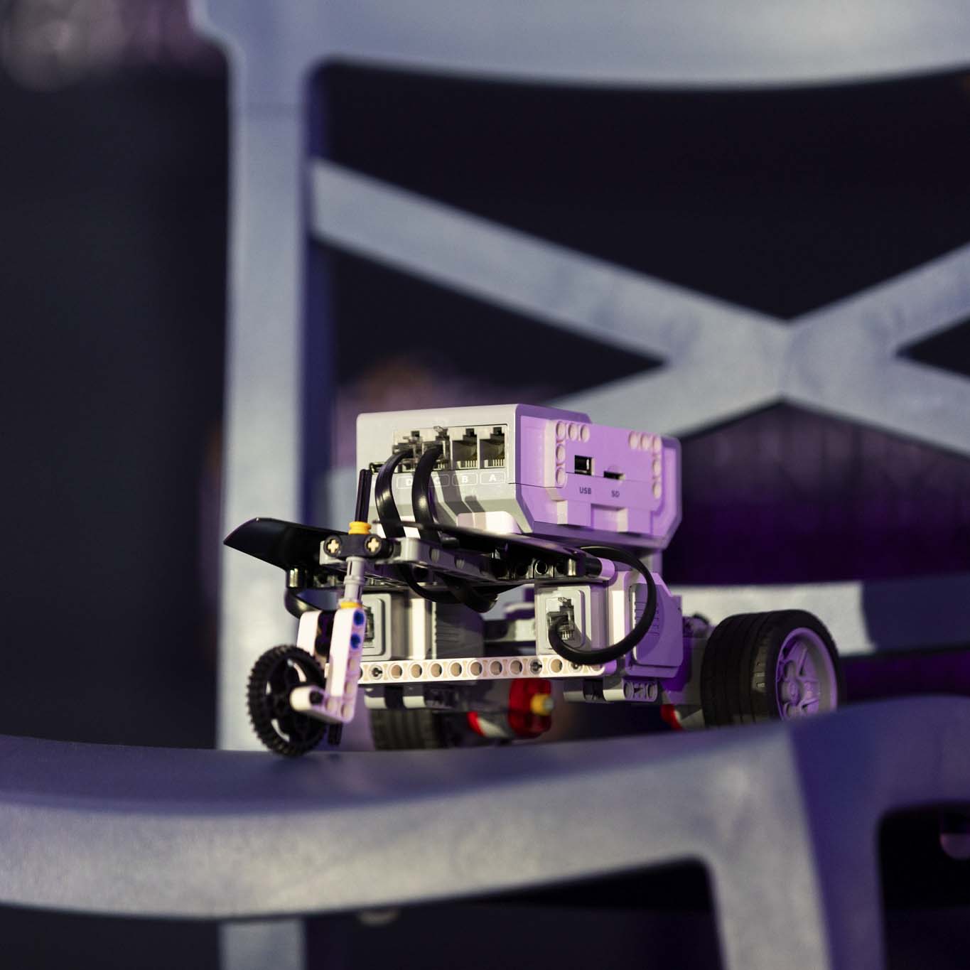 Na krześle postawiony jest robot. Niewielki, złożony z klocków, na trzech kołach.