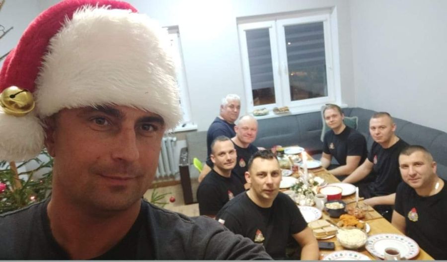 Zdjęcie grupowe strażaków z jednostki ratowniczo gaśniczej numer 3 w Pasłęku podczas wigilijnej kolacji. Strażacy zasiadają przy stole na którym stoją wigilijne potrawy.