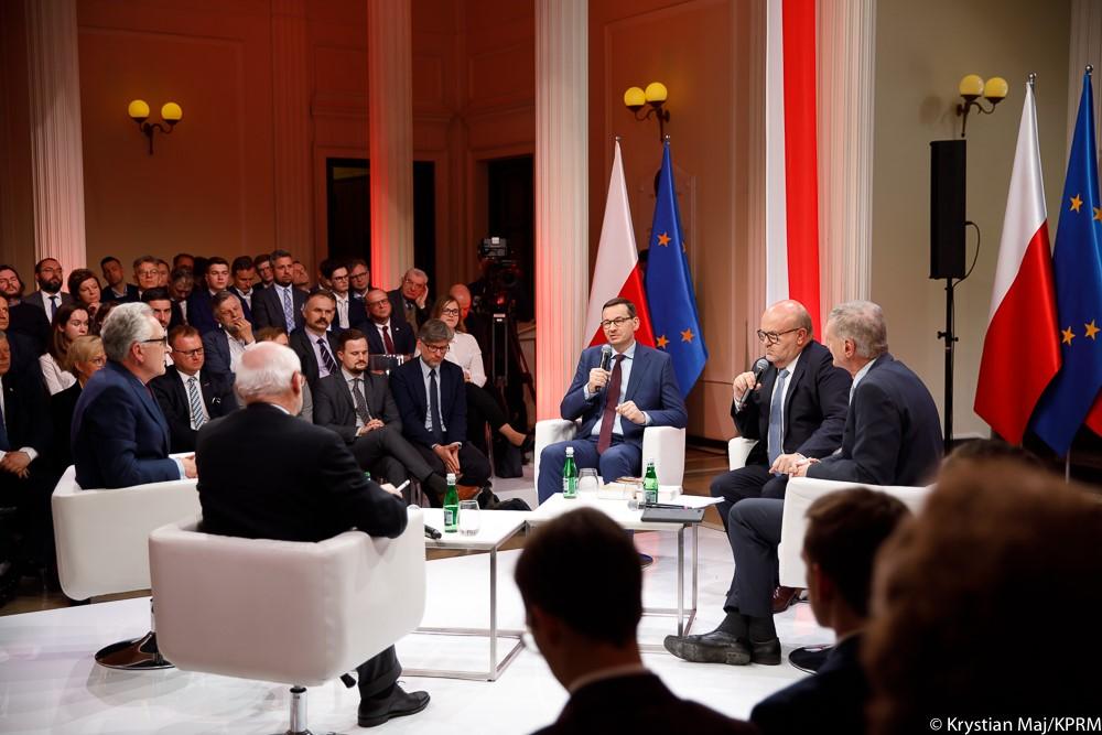 Premier Mateusz Morawiecki przy stole z panelistami podczas debaty.