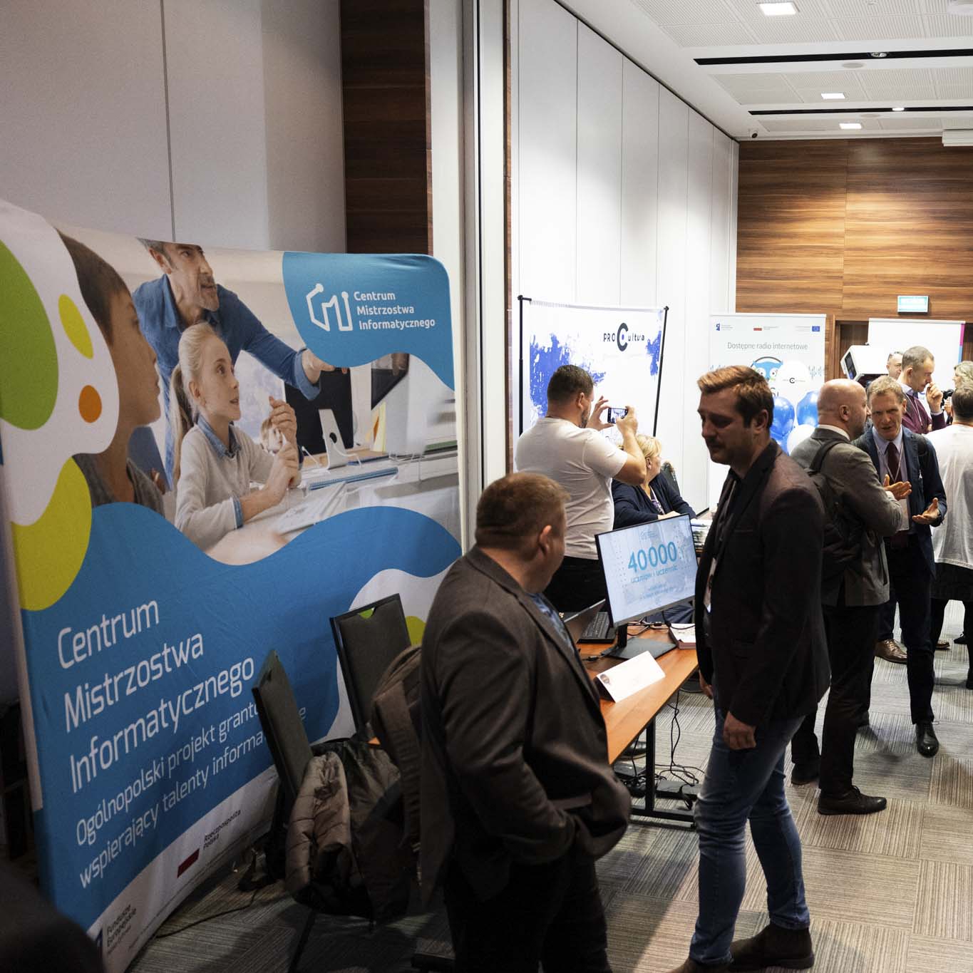 Uczestnicy konferencji rozmawiają przy stoiskach beneficjentów.