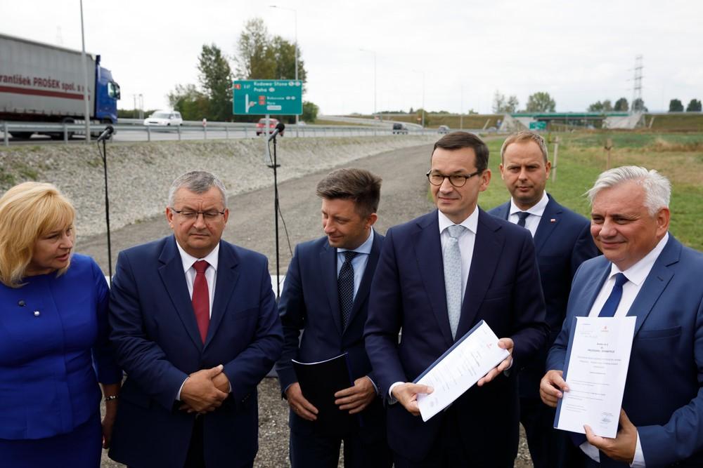 Premier Mateusz Morawiecki, minister Michał Dworczyk, Minister Andrzej Adamczyk i lokalni działacze trzymają podpisane umowy.
