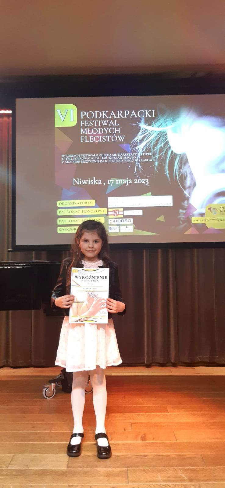 Uczennica trzymająca dyplom wyróżnienia I stopnia. Z tyłu widać fortepian.