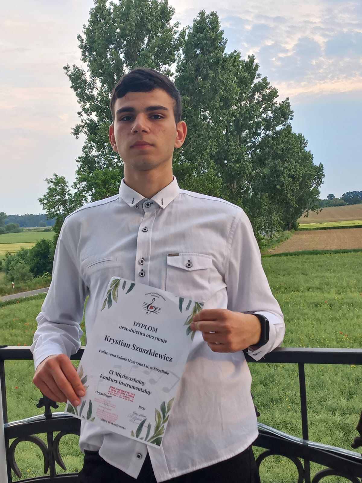 Na zdjęciu widoczny jest elegancko ubrany chłopiec, który trzyma w rękach dyplom konkursowy.