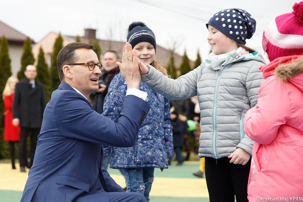 Premier Mateusz Morawiecki przybija piątkę z dziećmi.