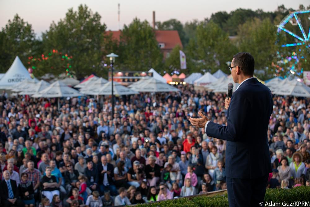 Premier na scenie mówi do tłumu ludzi.