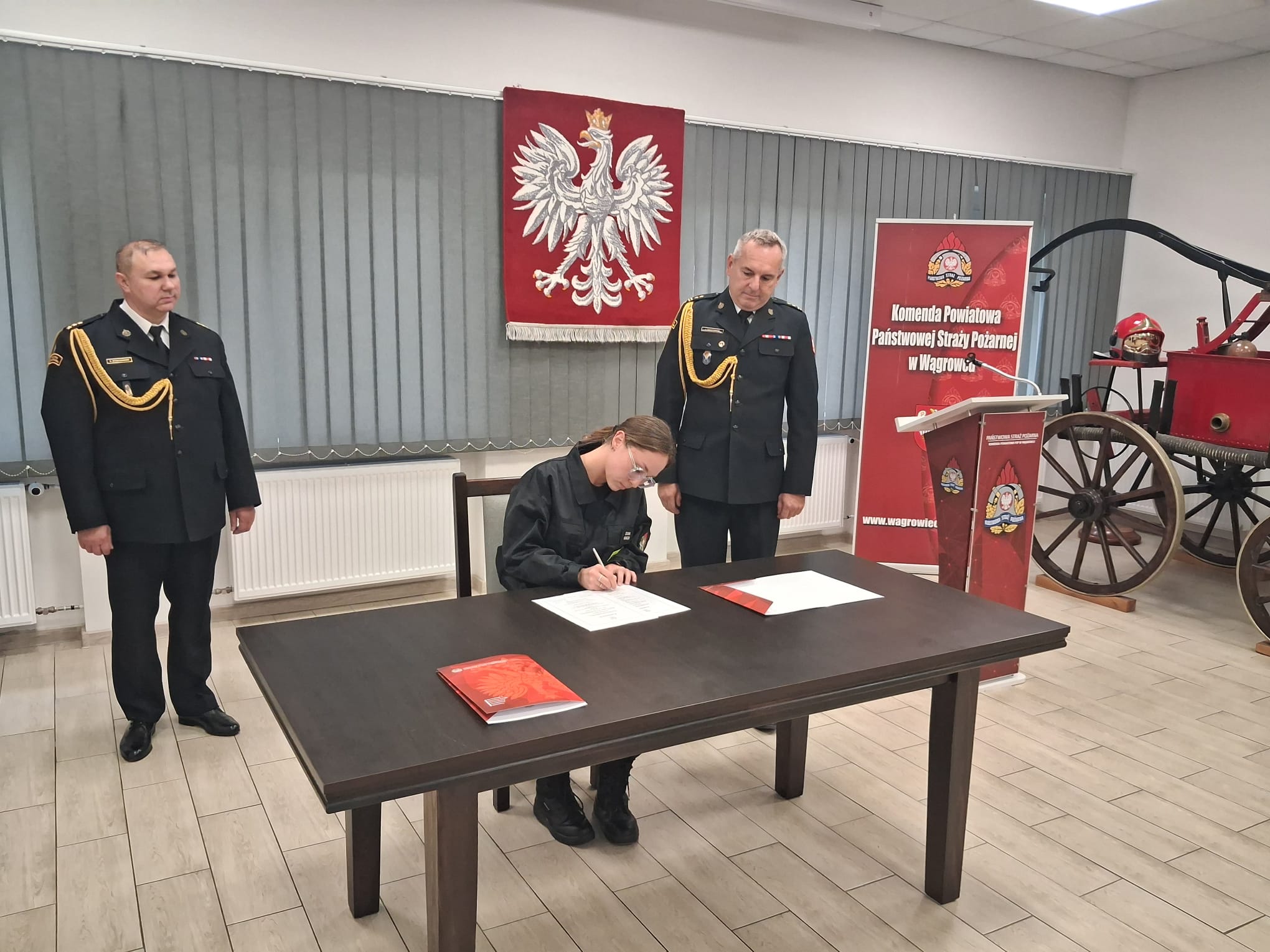 Na zdjęciu widać funkcjonariuszkę podczas podpisywania dokumentów w obecności kierownictwa Komendy Powiatowej PSP 