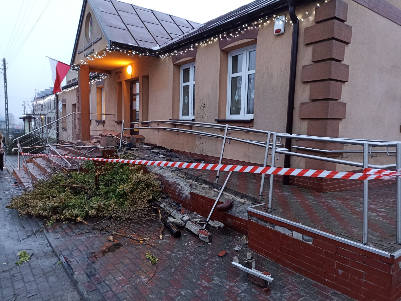 Uszkodzony budynek Gminnej Biblioteki Publicznej w Dalikowie. Zdjęcie przedstawia uszkodzone barierki, schody podjazd dla niepełnosprawnych i główne wejście. 