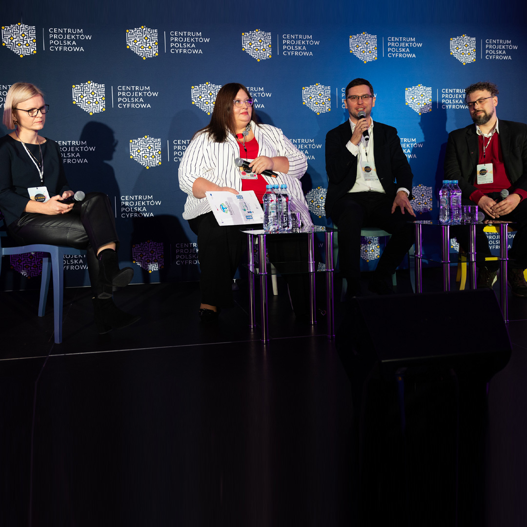 Czwórka panelistów siedzi na krzesłach na podium. Pan Daniel Duda mówi do mikrofonu, reszta uczestników słucha wypowiedzi.