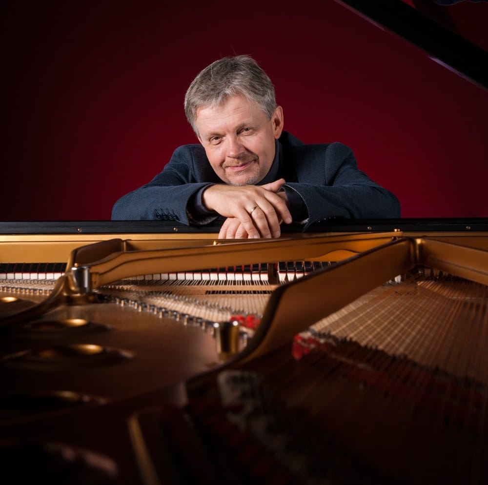 Mężczyzna siedzący przy fortepianie. Na pierwszym planie widoczne wnętrze instrumentu.