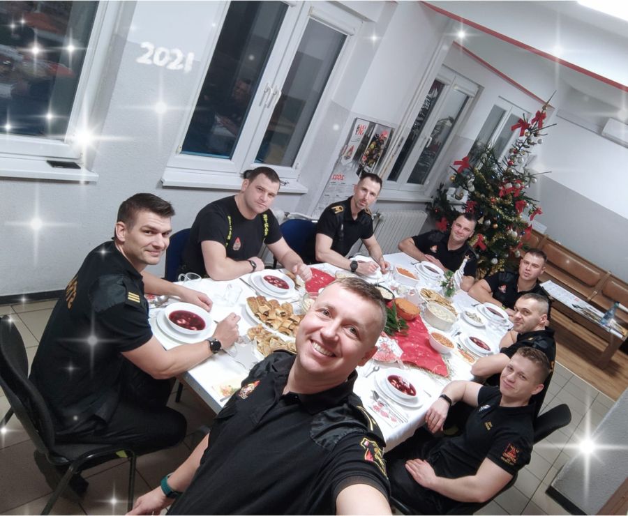 Zdjęcie grupowe strażaków z jednostki ratowniczo gaśniczej numer 2 w Elblągu podczas wigilijnej kolacji. Strażacy zasiadają przy stole na którym stoją wigilijne potrawy.