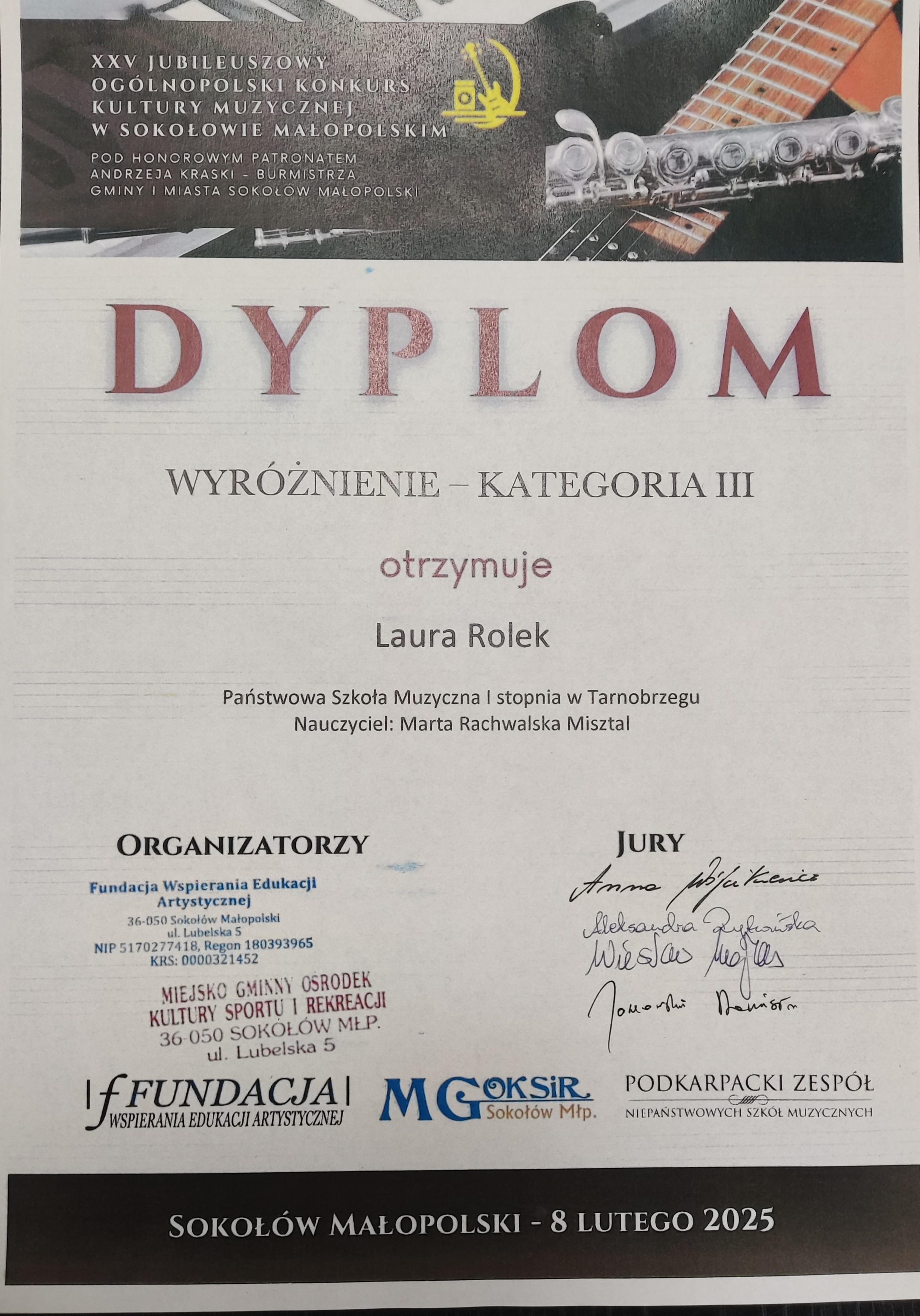 Dyplom wyróżnienia. Na górze znajduje się nazwisko patrona w brązowej ramce, a w tle zdjęcie przedstawiające fragmenty fortepianu, gitary oraz fleta poprzecznego. Po środku nazwisko otrzymującego wyróżnienie oraz nauczyciela. Na dole po lewej stronie organizatorzy, a po prawej podpisy jury. Tekst w kolorze czerwonym i czarnym.