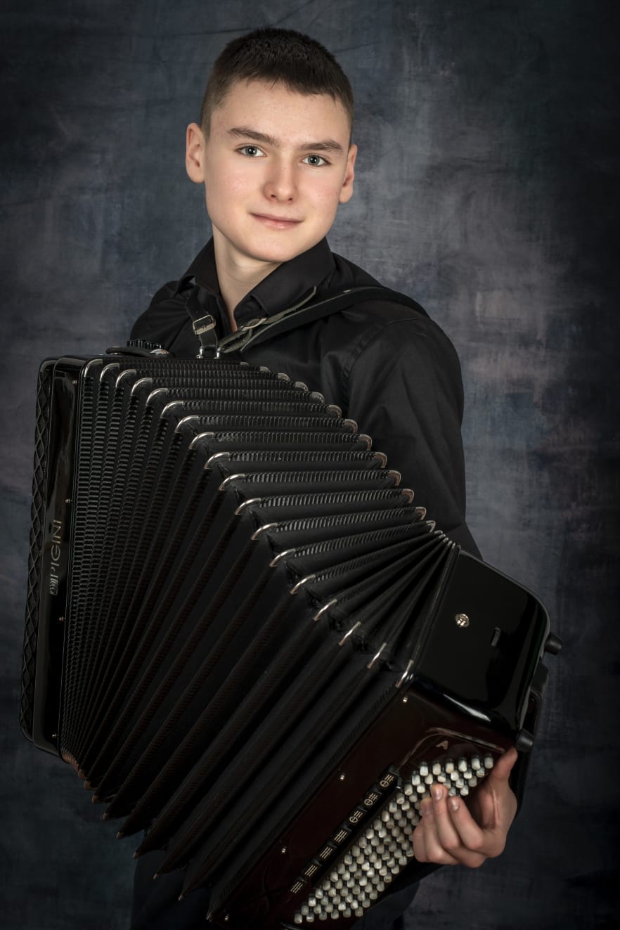 Zdjęcie - Matusz Neckar. Uczeń grający na akordeonie, czarne tło