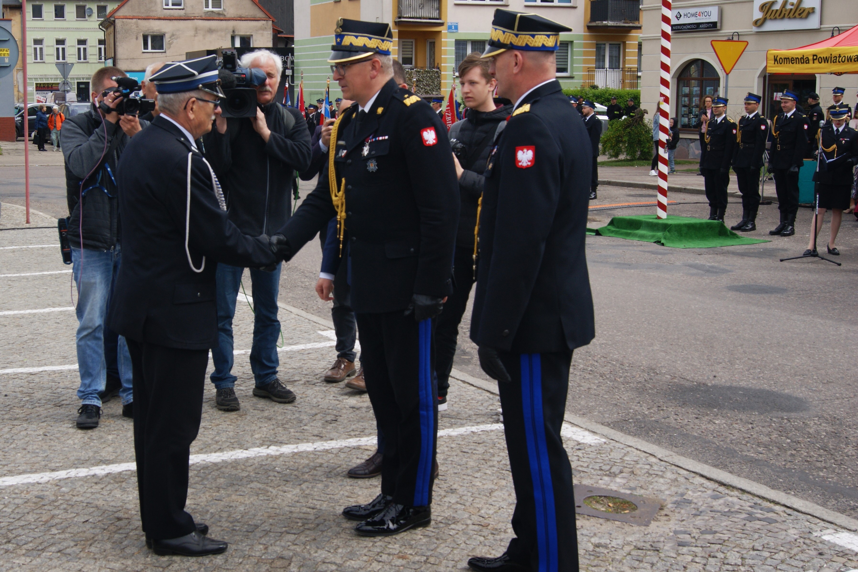 Zastępca komendanta głównego PSP podaje rękę druhowi OSP w geście gratulacji, obok komendanta stoi komendant wojewódzki