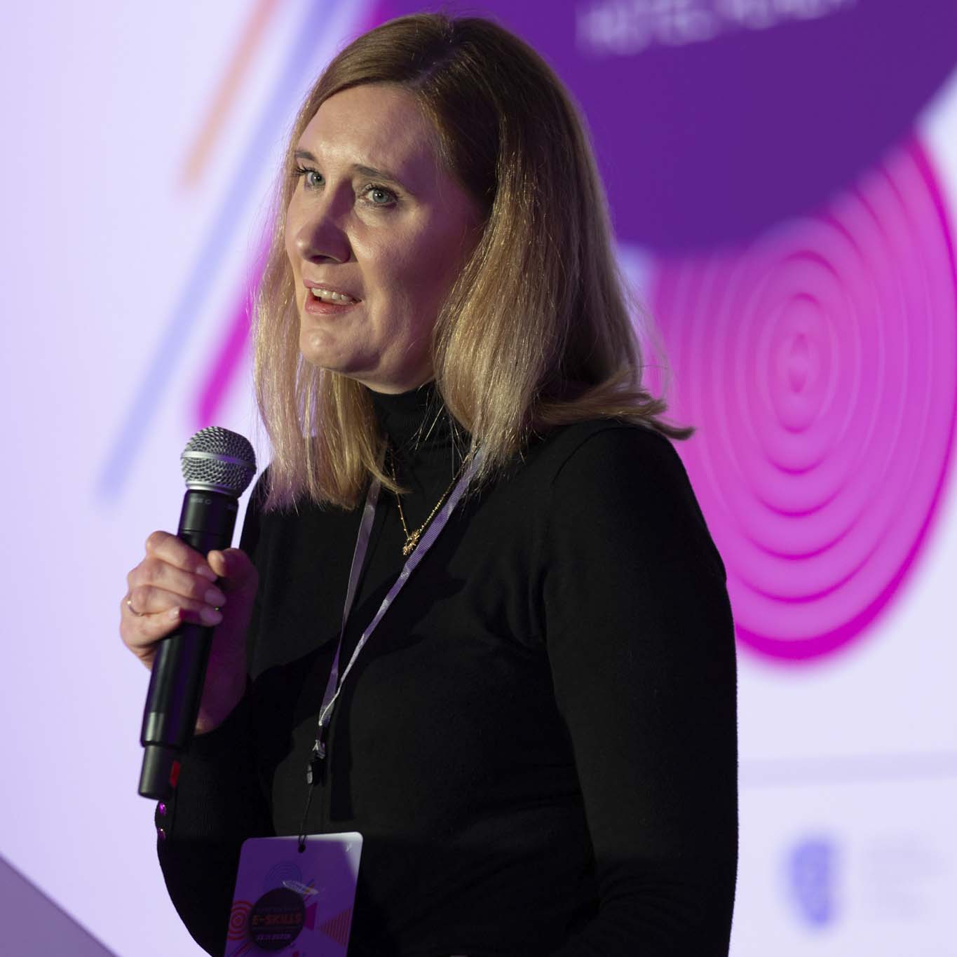 Pani Agnieszka Krauzowicz stoi na podeście i mówi do mikrofonu.