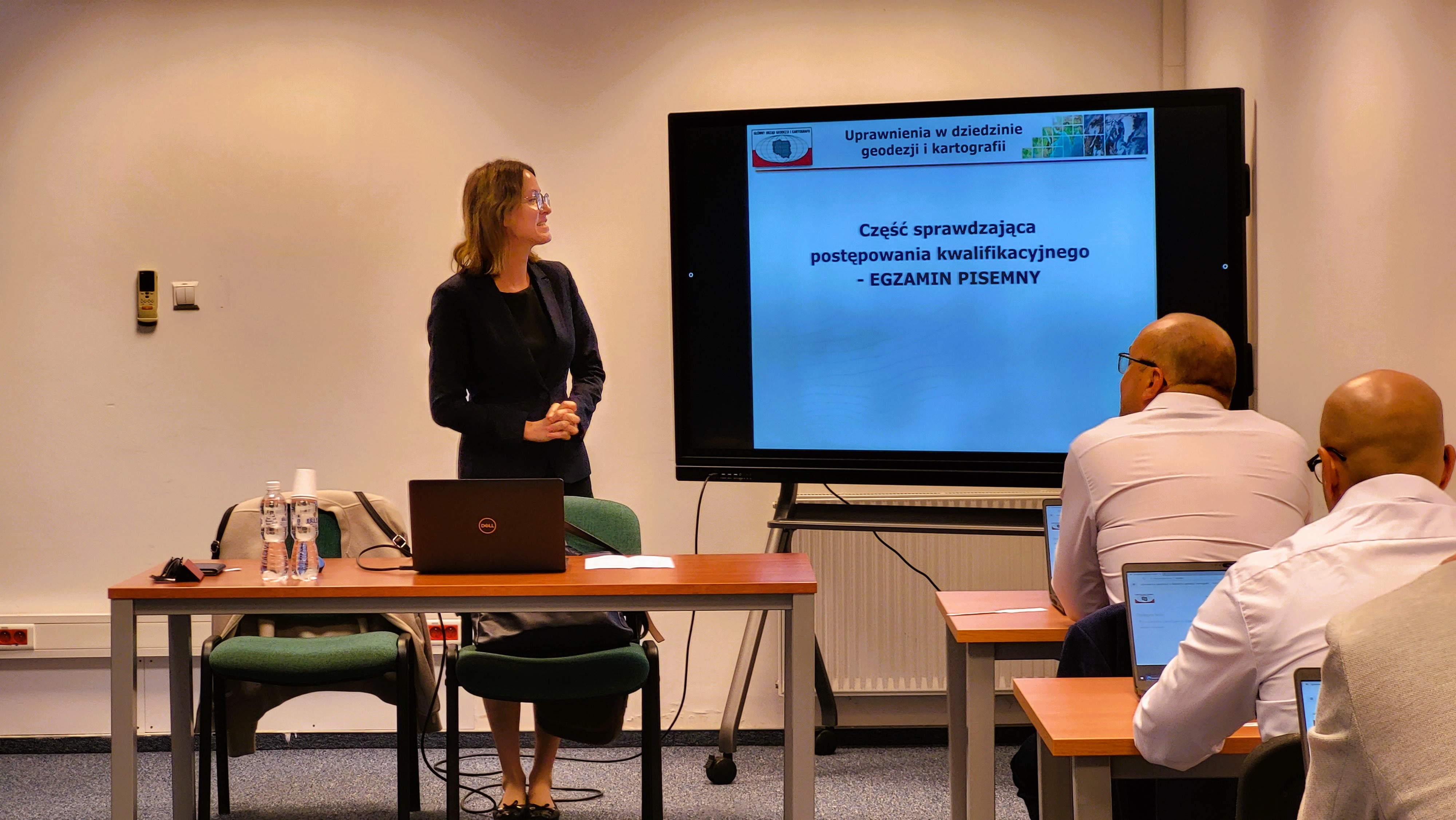 Zdjęcie przedstawia salę egzaminacyjną z członkami Komisji egzaminacyjnej i osobami przystępującymi do egzaminu siedzącymi pojedynczo przed laptopami