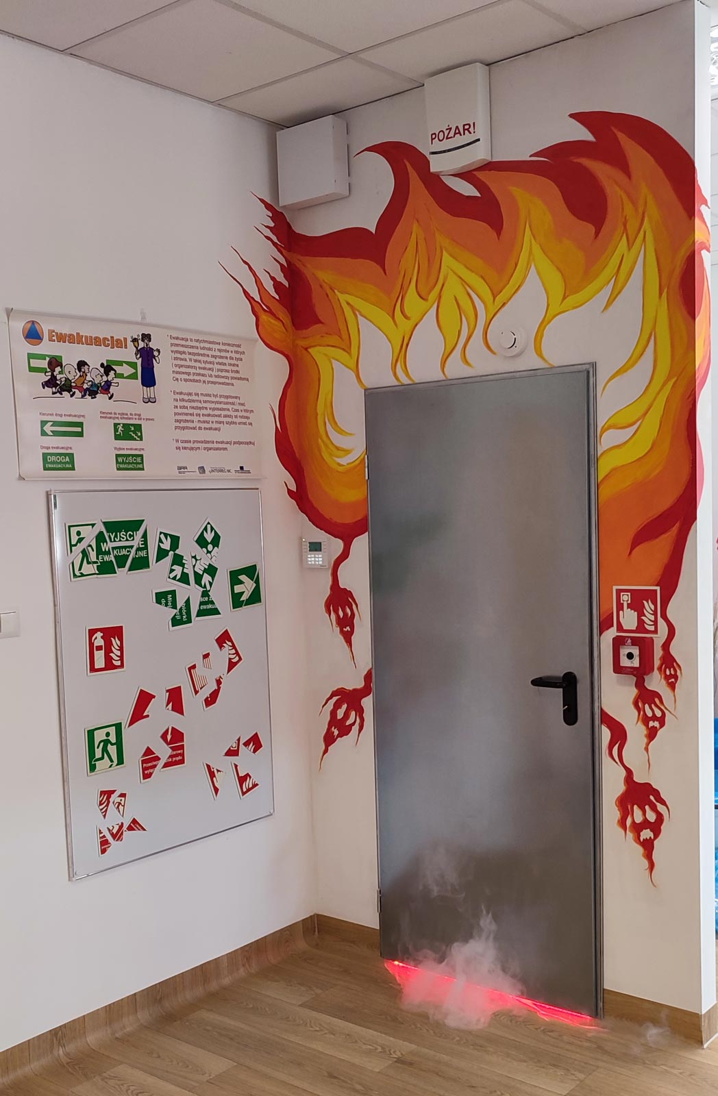 Stanowisko gorących drzwi oraz znaki ewakuacyjne w Sali Ognik w Komendzie Powiatowej Państwowej Straży Pożarnej w Lublińcu
