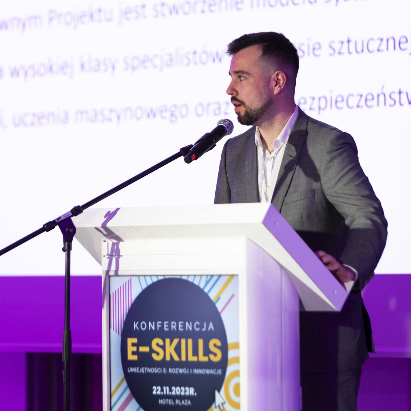 Przy mównicy stoi Pan Michał Mucha. Wzrok kieruje w stronę uczestników konferencji. Mówi do mikrofonu.