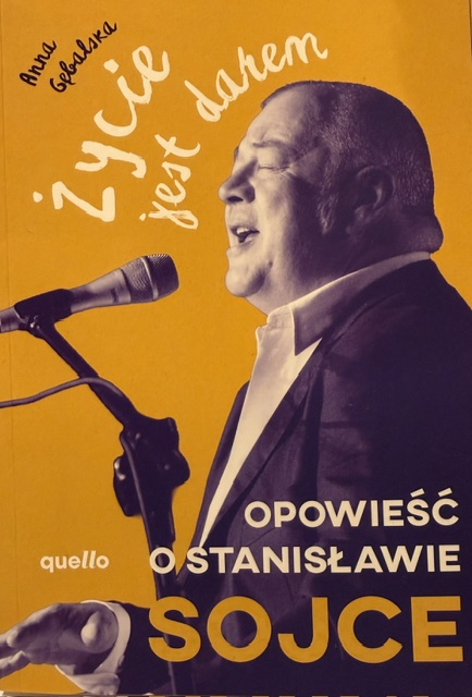 Okładka książki Anny Gębalskiej 'Życie jest darem. Opowieść o Stanisławie Sojce' ze zdjęciem śpiewającego artysty przed mikrofonem.