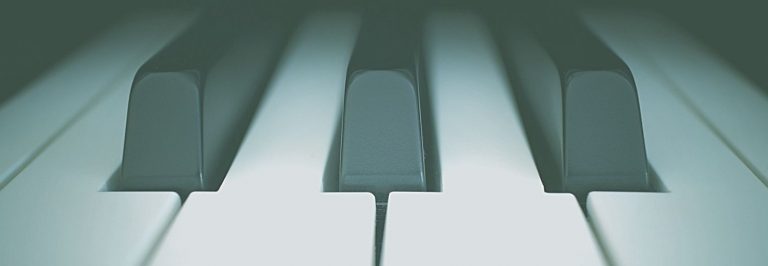 Zdjęcie. Duże zbliżenie przedstawiające część klawiatury fortepianu lub pianina Widoczne cztery białe oraz trzy czarne klawisze