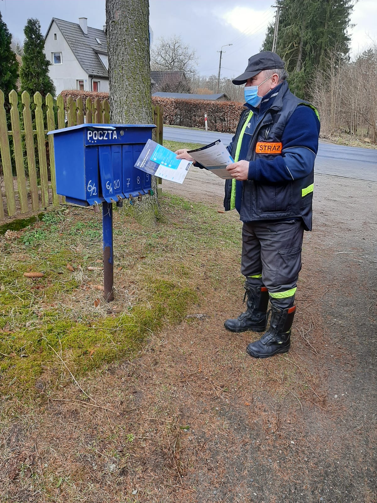 Zdjęcie przedstawia strażaka wkładającego do niebieskich skrzynek pocztowych ulotki.