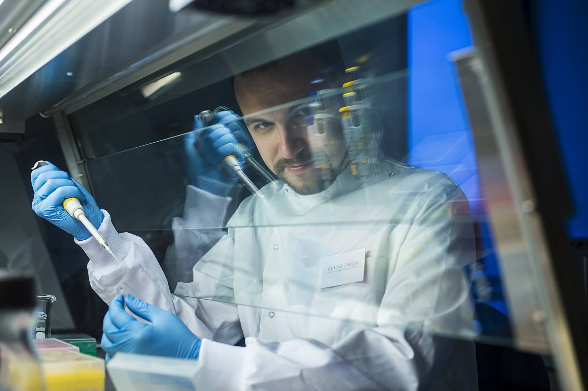 Doktor habilitowany Adam Kuzdraliński, Uniwersytet Przyrodniczy w Lublinie, podczas pracy w laboratorium. W białym kitlu i niebieskich rękawiczkach, za szybą