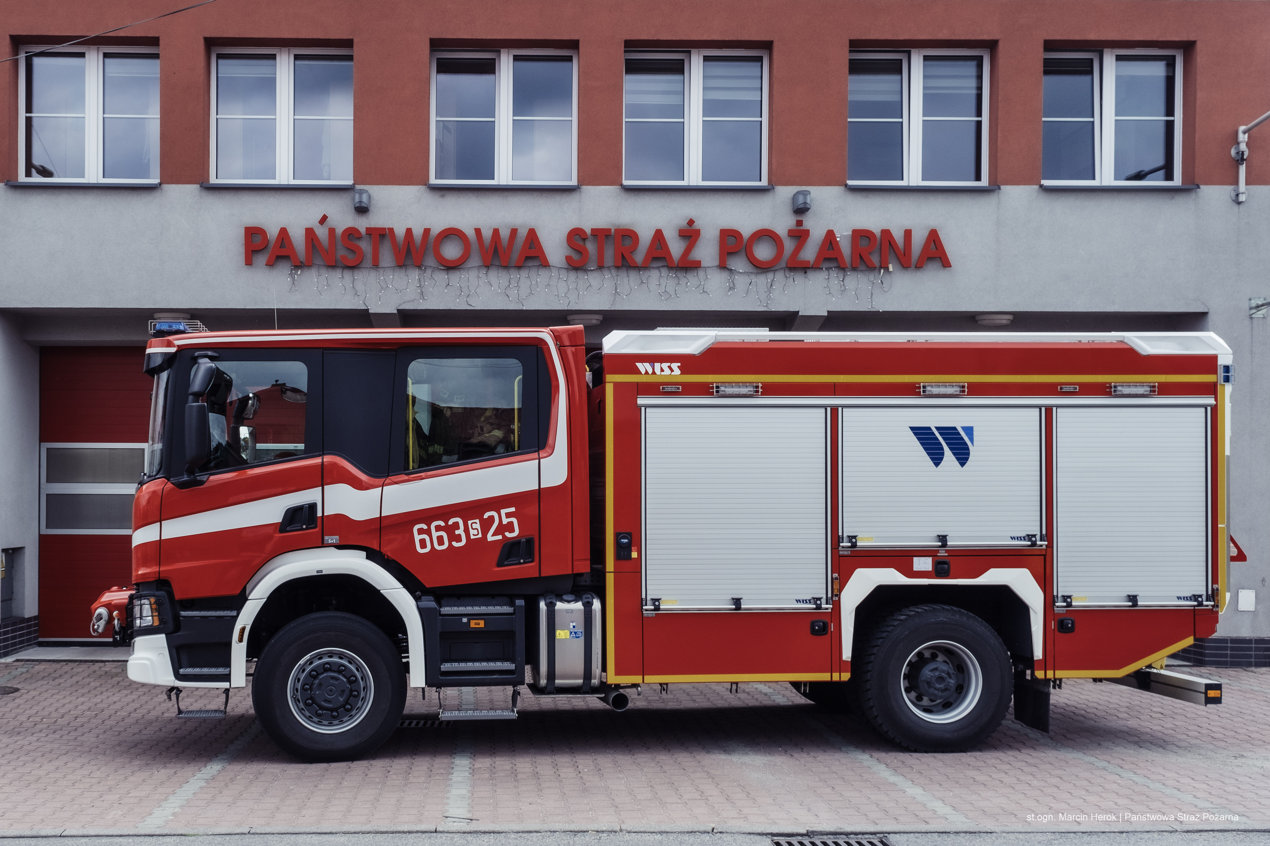 Zdjęcie przedstawia ciężki samochód ratowniczo-gaśniczy. W tle budynek Jednostki Ratowniczo-Gaśniczej w Rydułtowach.