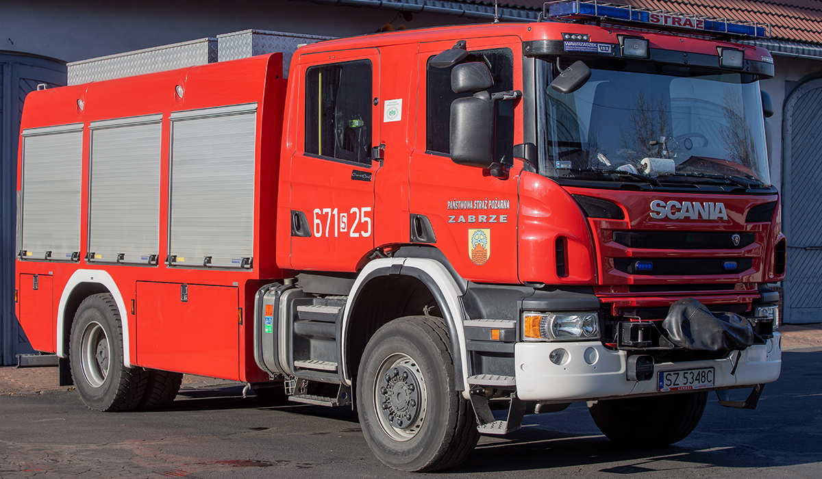 Zdjęcie przedstawia samochód ratowniczo-gaśniczy - ciężki Scania P400 na tle budynku Komendy Miejskiej Państwowej Straży Pożarnej w Zabrzu