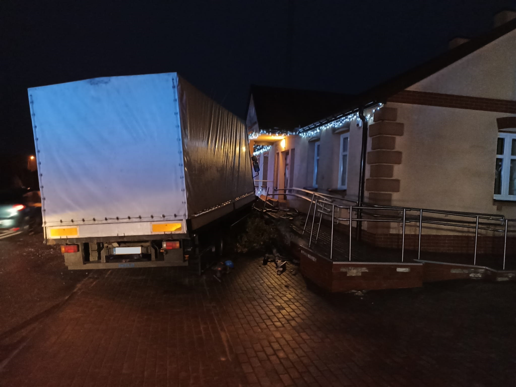 Po lewej stornie zdjęcia znajduje się tylna część samochodu ciężarowego stojący na chodniku, przednia część pojazdu uszkodziła budynek Gminnej Biblioteki Publicznej w Dalikowie 