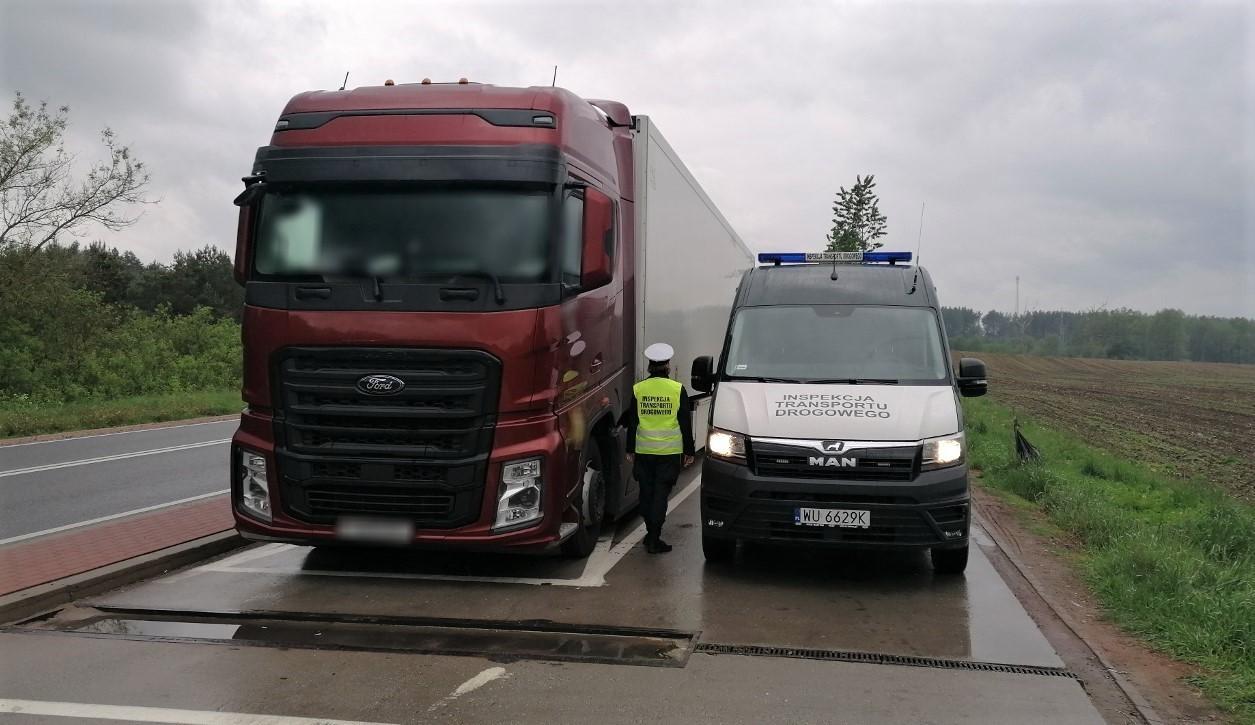 Inspektor i radiowóz ITD stoją koło zatrzymanej do kontroli ciężarówki.
