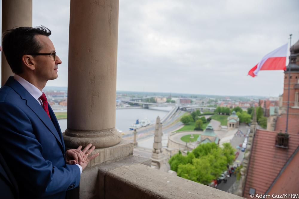 Po lewo premier stoi na balkonie, a po prawo widok na flagę Polski, która została wciągnięta na Urząd Wojewódzki.