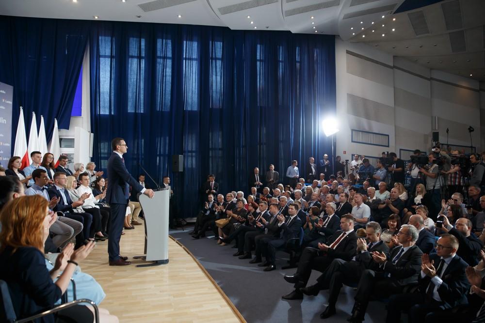 Premier Mateusz Morawiecki przemawia przy mównicy na sali pełnej mieszkańców.
