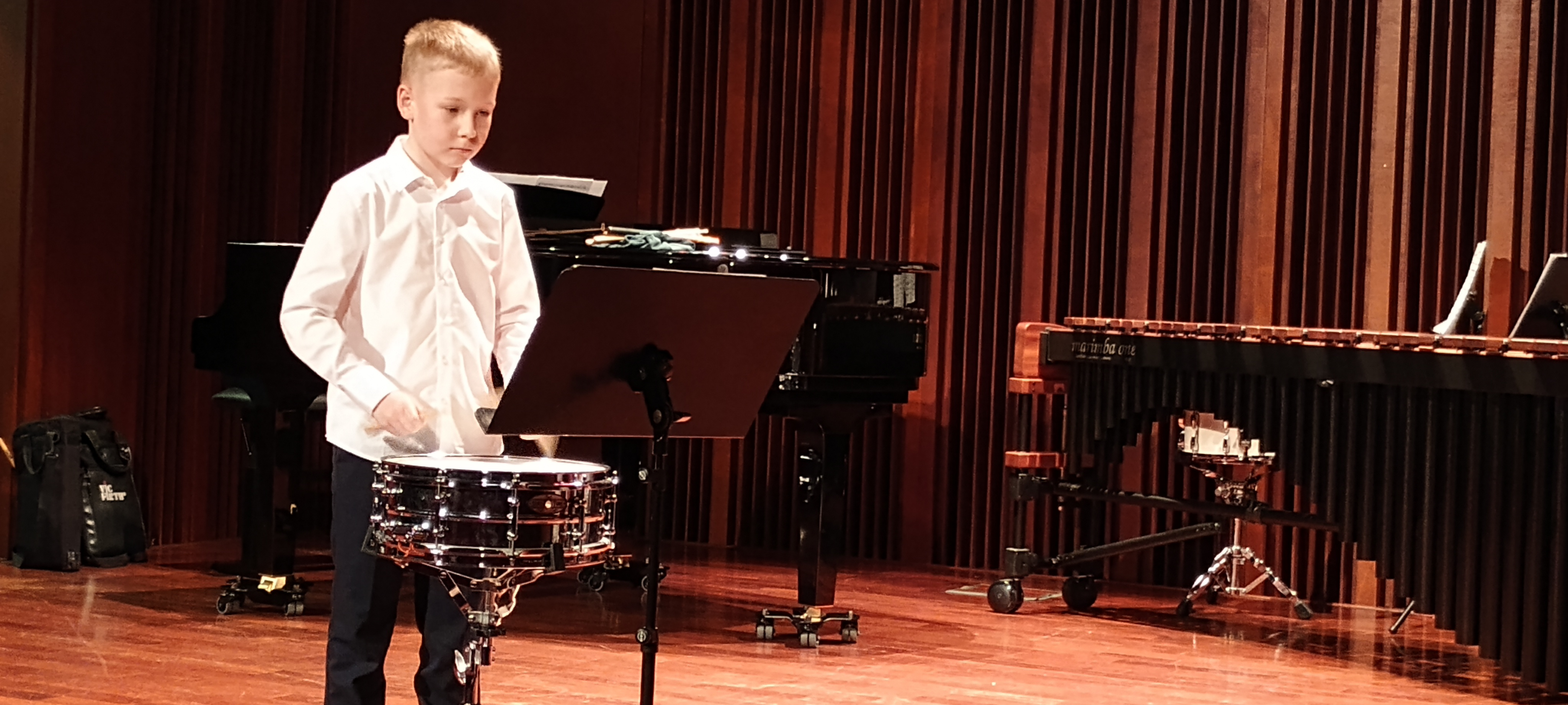 Warsztaty perkusyjne w szkole. Uczeń gra na werblu na scenie sali koncertowej.