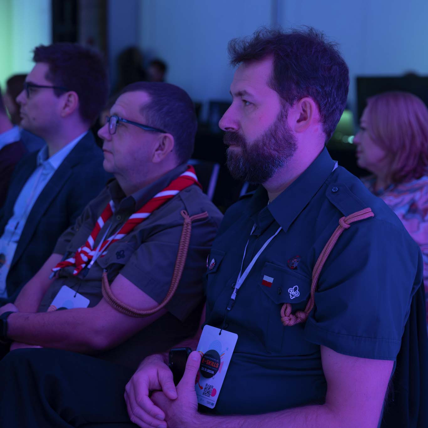 Na krzesłach siedzą uczestnicy i uczestniczki konferencji. Wzrok kierują w stronę sceny.