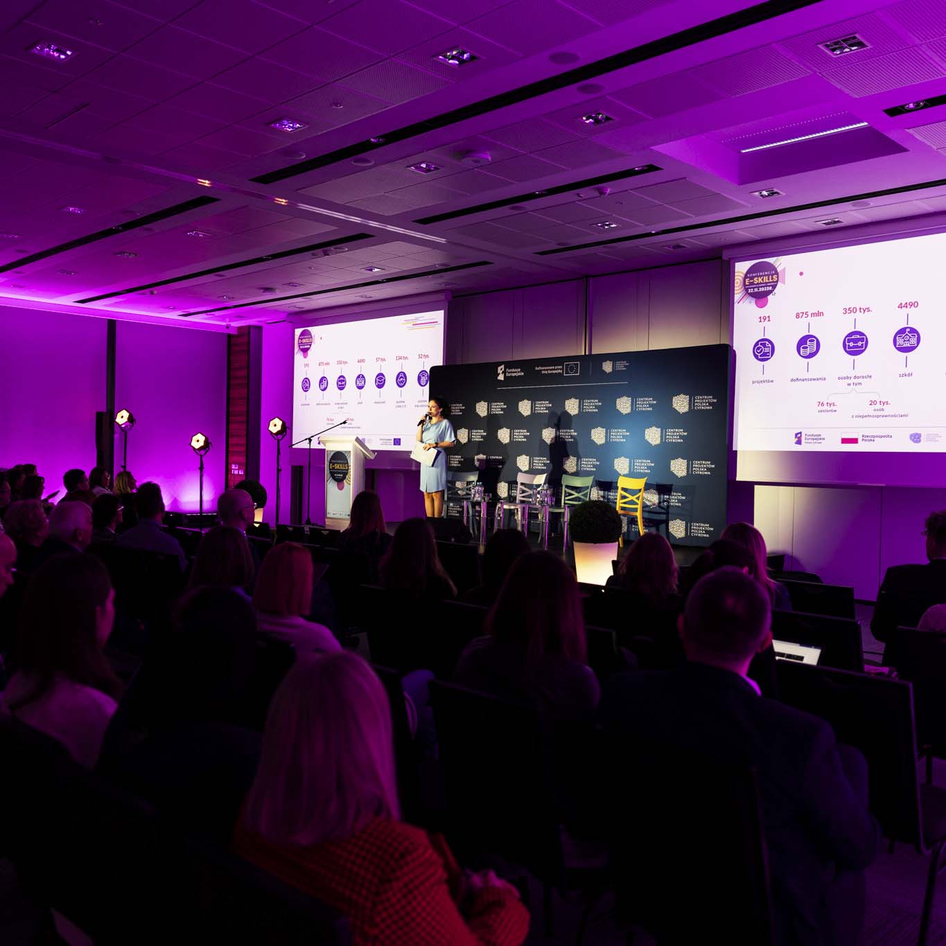 Pani Anna Butrym stoi na środku podium trzyma w ręku mikrofon. Wzrok kieruje na uczetników konferencji.