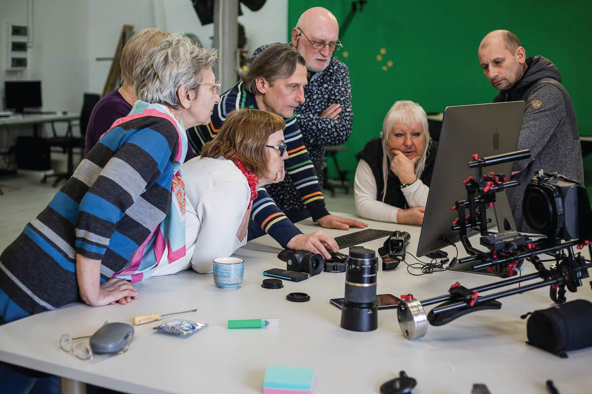 Sześcioosobowa grupa seniorów pracuje przy stole inżynierskim pod okiem prowadzącego zajęcia