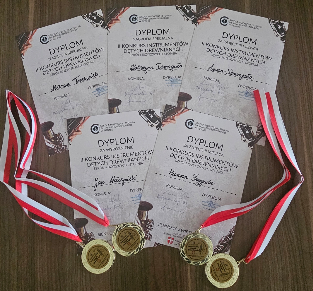 Pięć dyplomów ułożonych na drewnianym blacie, przyznanych za udział w II Konkursie Instrumentów Dętych Drewnianych Szkoły Muzycznej I Stopnia im. Jana Chorosińskiego w Siennie. Każdy dyplom zawiera imię i nazwisko laureata oraz podpisy komisji i dyrekcji. Obok dyplomów leżą trzy złote medale zawieszone na czerwono-białych wstążkach, symbolizujących osiągnięcia i wyróżnienia.