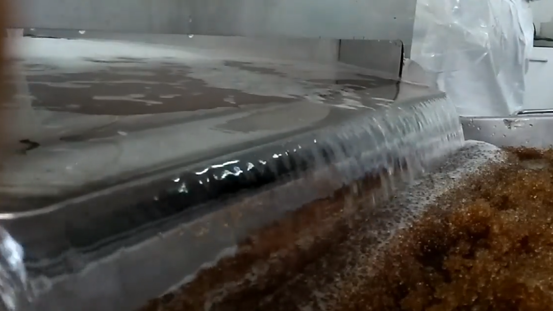 A two-stage metal construction from which transparent water flows onto the brown-colored bio-substrate