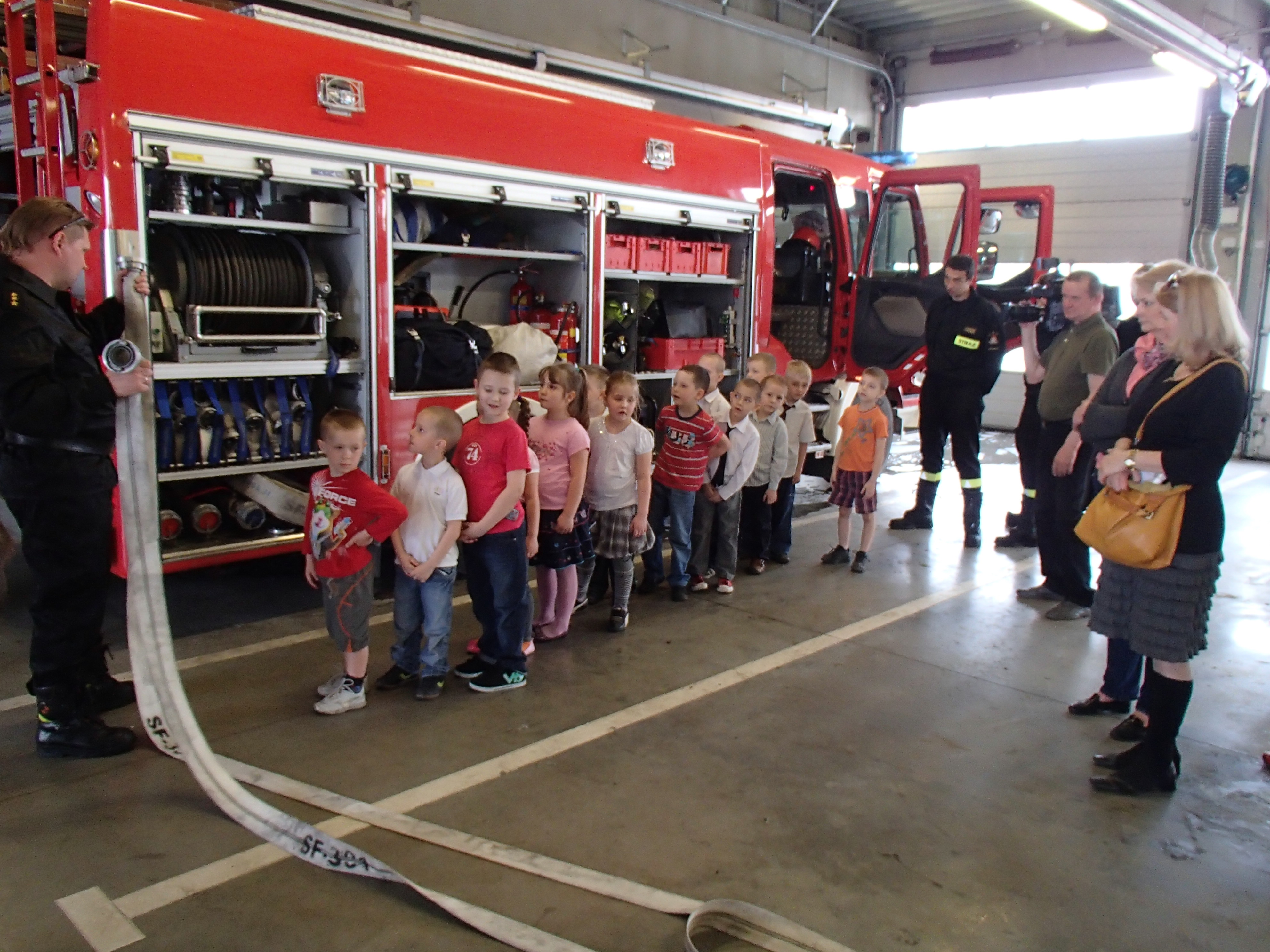 wóz strażacki , dzieci oglądające rozwijanie węża strażackiego