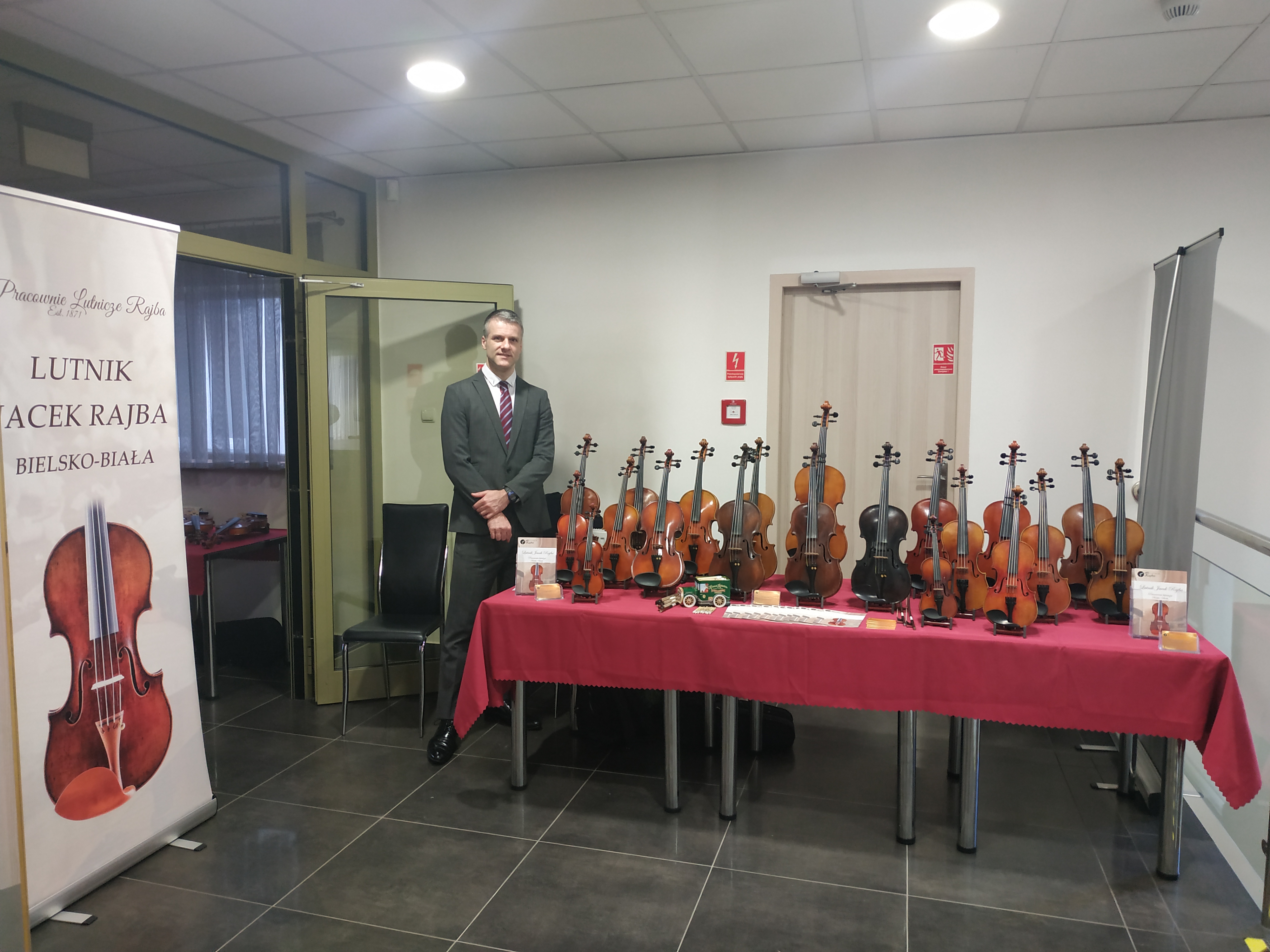 Zdjęcie lutnika Jacka Rajby przedstawiającego swoją kolekcję skrzypiec.