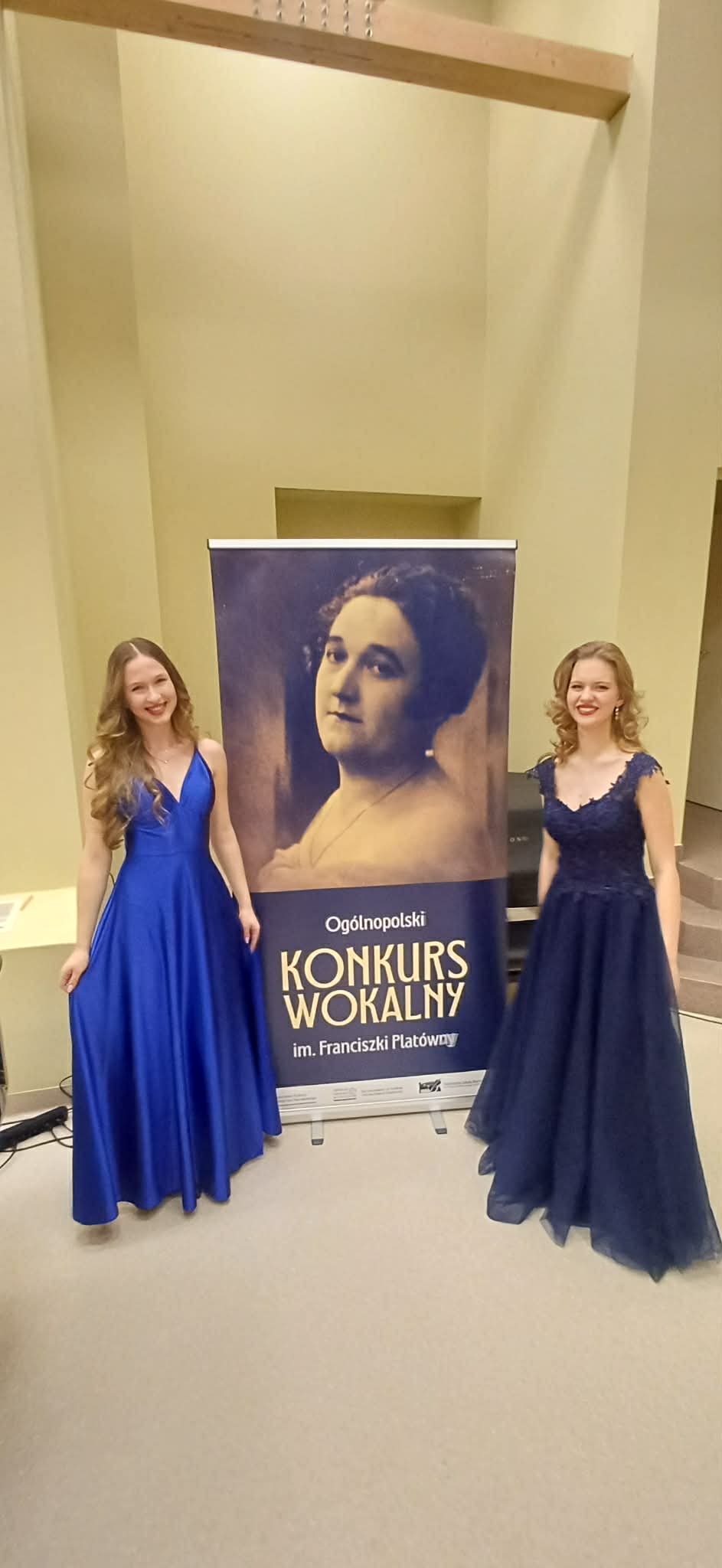  Amelia Szmidt (z lewej) Konkurs Wokalny Wrocław 2026. Obok druga wokalistka. Panie ubrane w niebieskie sukienki, w tle baner konkursu.