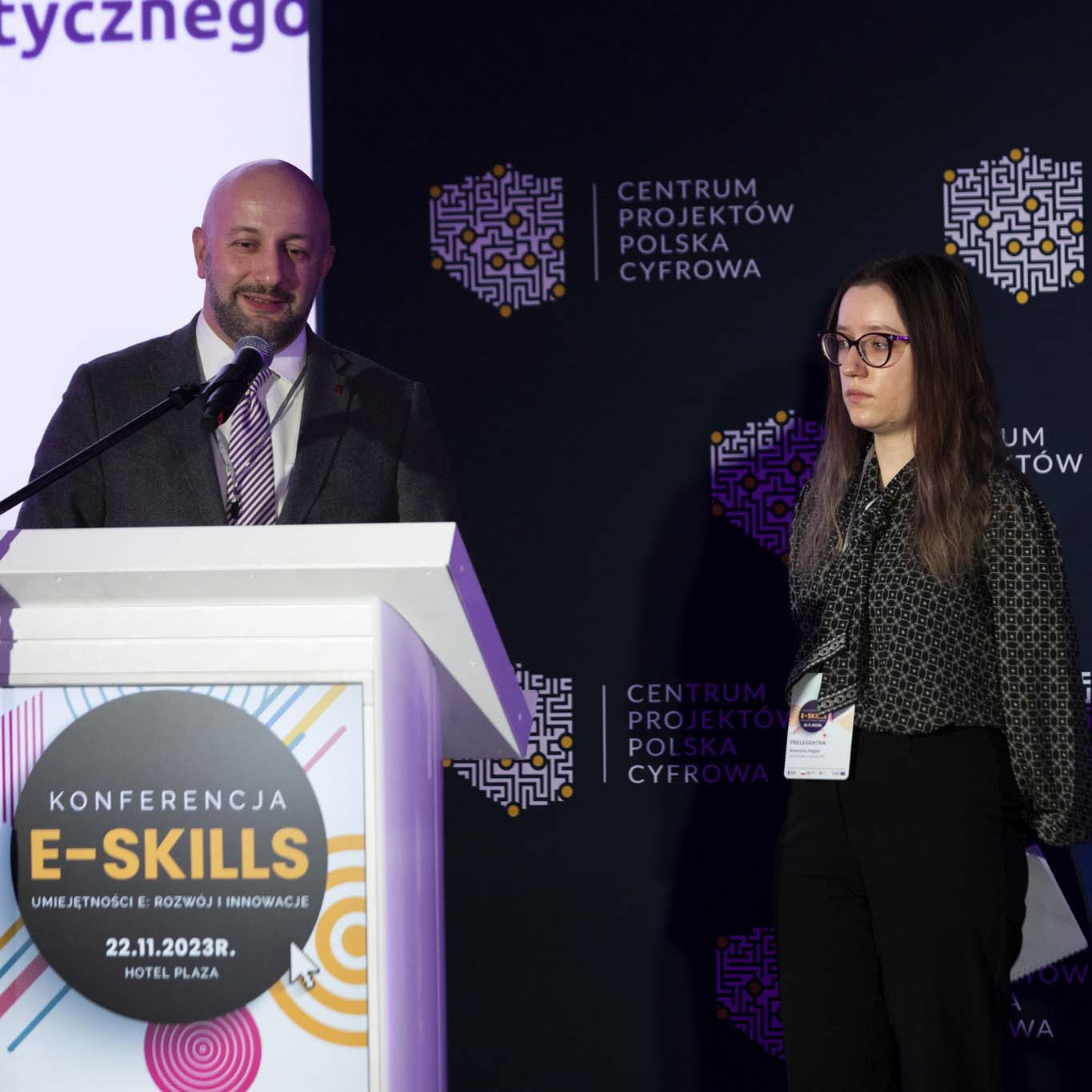 Przy mównicy stoi Pan Hubert Gęsiarz, obok niego stoi Pani Antonina Negler i doktor inżynier Maciej Sajkowski.